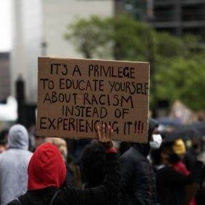 A protester holding a banner saying "It's a privilege to educate yourself about racism instead of experiencing it"