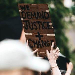 A protester holding a banner saying "we demand justice + change"