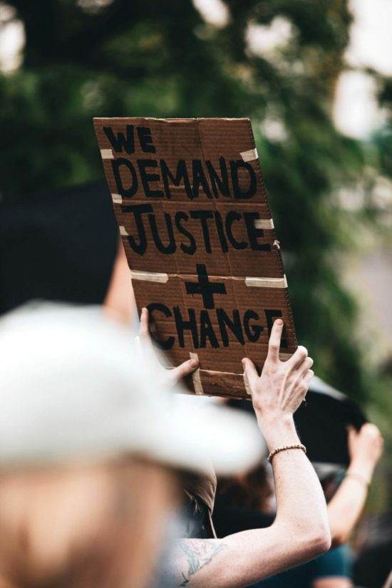 A protester holding a banner saying "we demand justice + change"